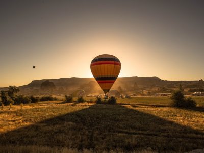 A picture of a colorful hot air balloon in a field surrounded by greenery and mountains during sunset